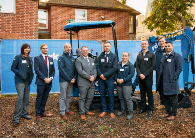 A group of people at a groundbreaking ceremony, standing in front of a digger