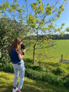 Picture of Lydia Smith (Regular Giving Officer) holding her puppy Lemon, both facing away from camera and out to a field on a sunny day.