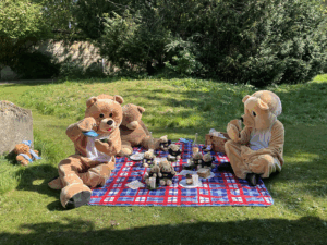 Two Teddy Bear Mascots having a picnic on a blanket with toy teapots, cups, in the sunshine